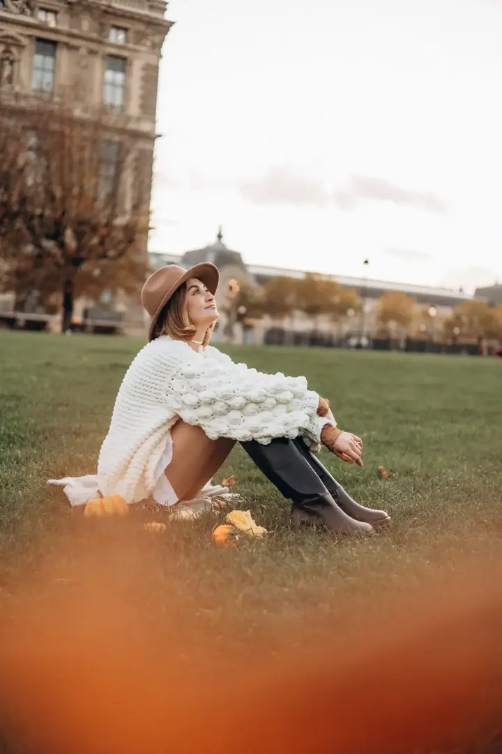 Woman white sweater hat sitting grass Louvre garden Paris